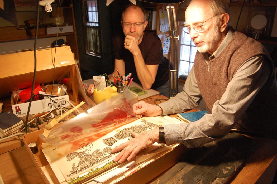 Ed Emberley (right), with his son Michael, leafs through a box of original art for “Drummer Hoff” in a studio in his Ipswich home. (Greg Cook)