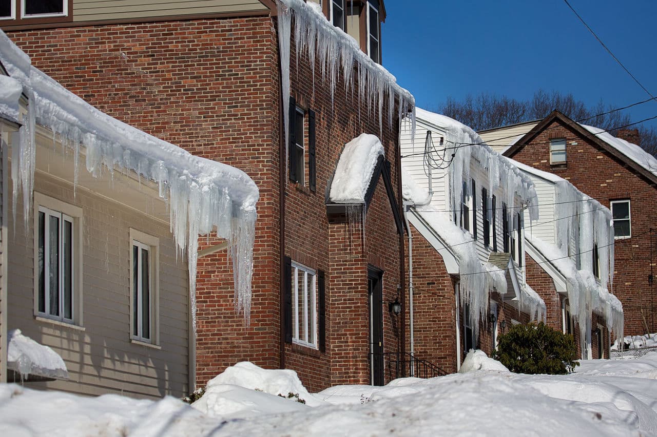 Huge banks of snow hindered many potential homebuyers from getting to know neighborhoods and finding parking spaces around homes for sale. In this photo taken last month, icicles hang from homes buried in snow along Itasca Street in Mattapan. (Jesse Costa/WBUR)
