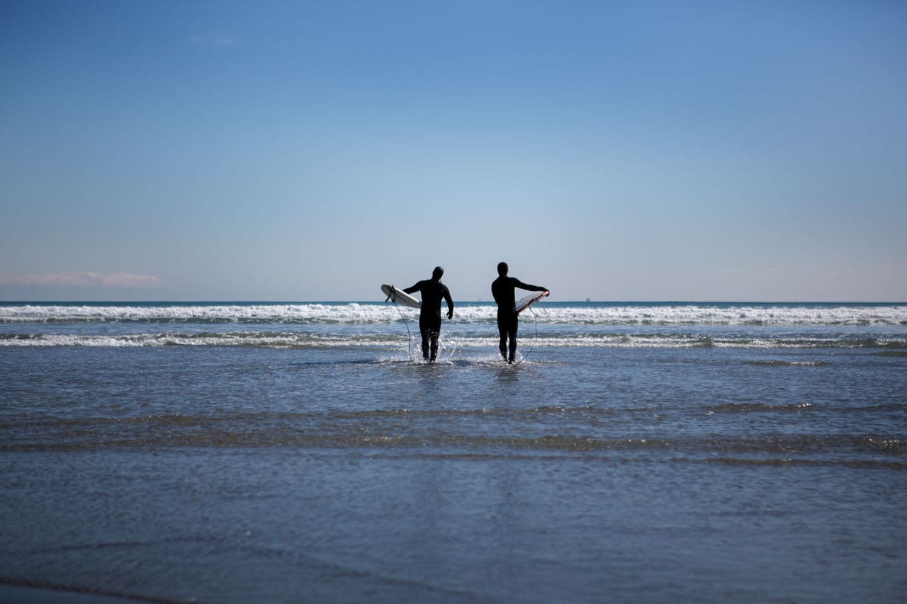 Tony Sanchez and Pat Falco heading out to surf on King’s Beach in Lynn on Nahant Bay. (Jesse Costa/WBUR)
