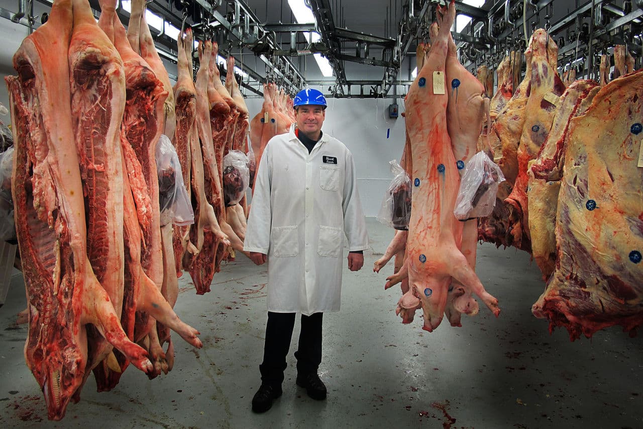 Dick Blood, the sixth generation of Bloods to work at Blood Farm, stands among pork and beef hanging in the refrigerator waiting to be processed. (Andrea Shea/WBUR)