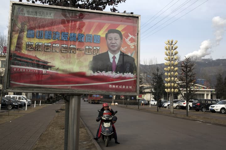 In this photo taken Feb. 6, 2015, a motorcyclist speaks on his phone near a billboard showing Chinese President Xi Jinping with the slogan "To exactly solve the problem of corruption, we must hit both flies and tigers" in Gujiao in northern China's Shanxi province. (AP)