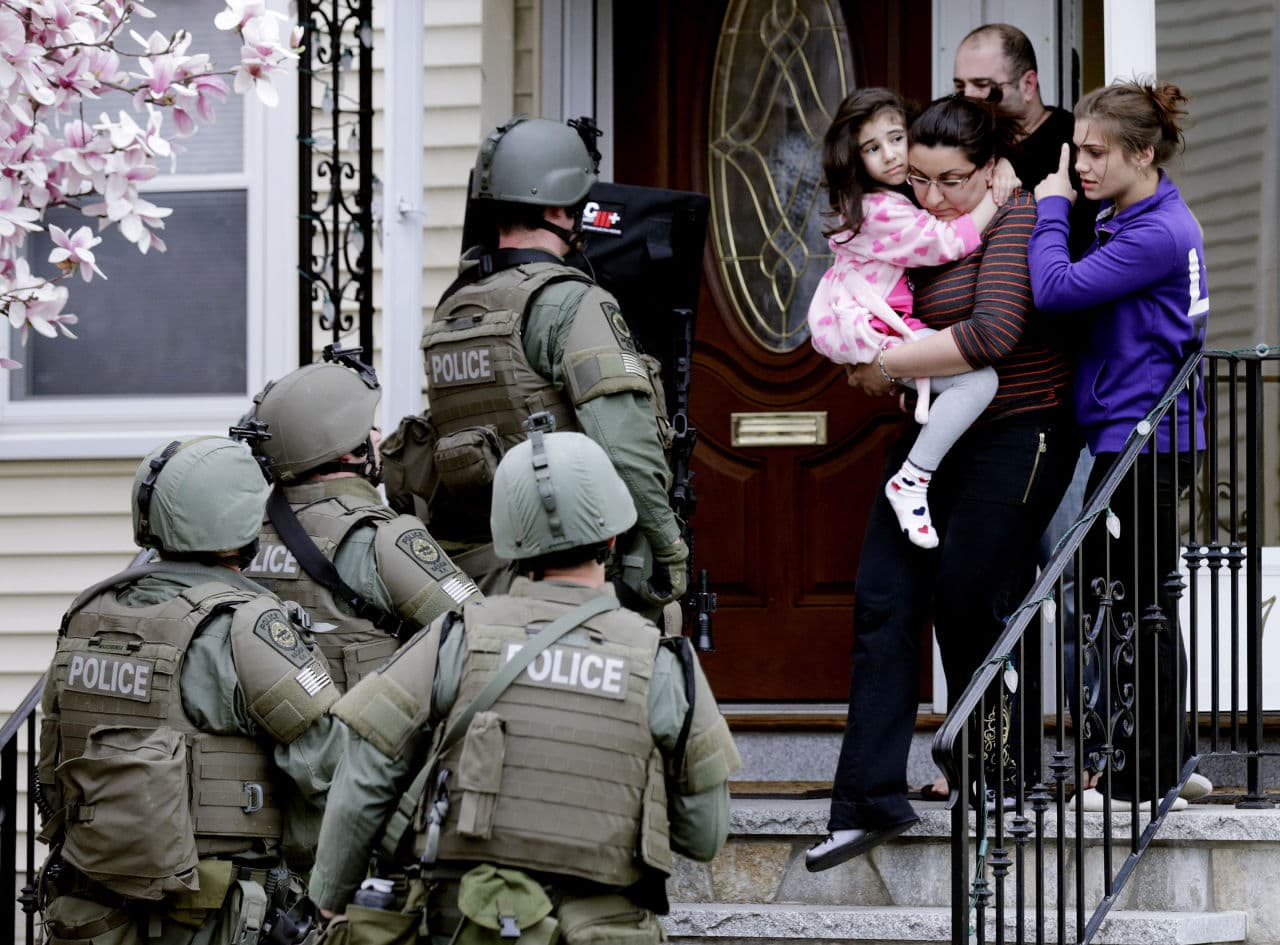 In this April 19, 2013, file photo, a woman carries a girl from their home as a SWAT team searching for a suspect in the Boston Marathon bombings enters the building in Watertown, Mass. (AP)
