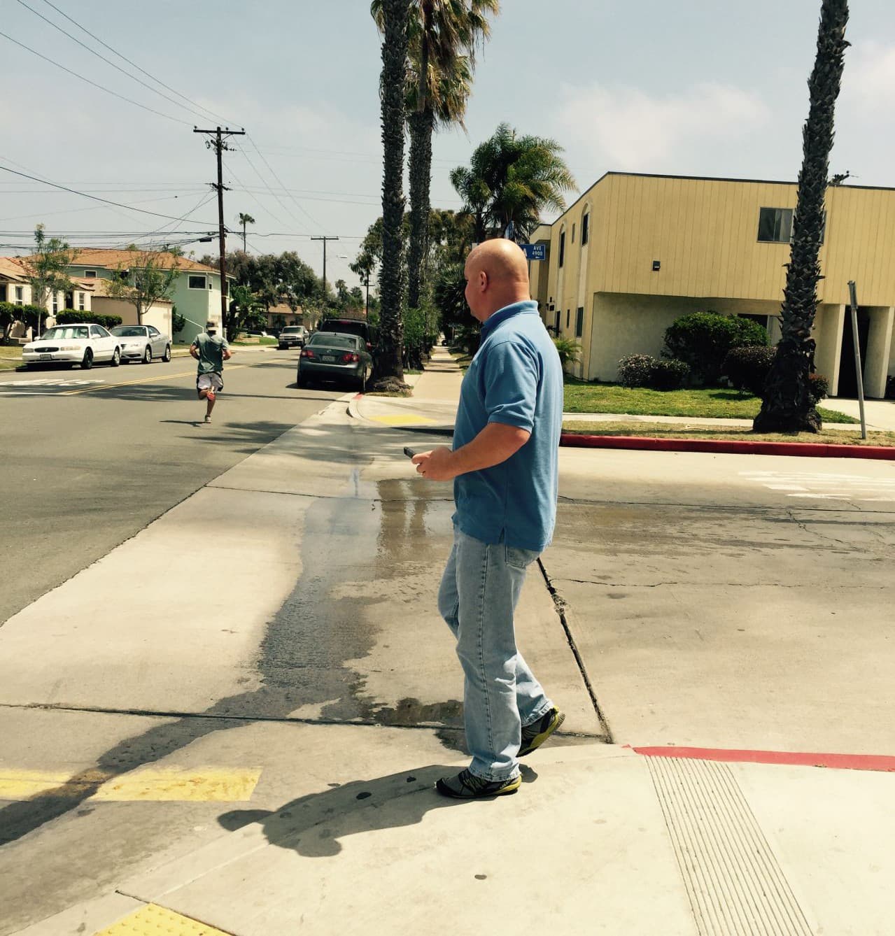 Chris Gehrki looks for the source of some water on the side of the road in San Diego. (Robin Young)