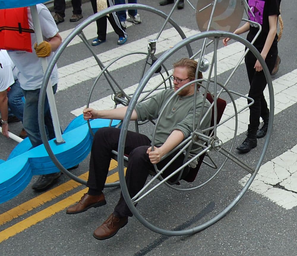 Wheel #2” was made by Bill Wainwright for the 1982 sculpture race and will be entering the permanent collection of the MIT Museum on Monday, race organizer Christian Herold said. His nephew, James Herold, who piloted it today, said, “It’s kind of like a cantilevered wheelchair with just two wheels. You have these smaller hand wheels that you move to go. It’s got a 0-degree turning radius. You can get up to some pretty significant speeds in this but the faster you go, the less control you have so you really don’t want to do that.” (Greg Cook/WBUR)