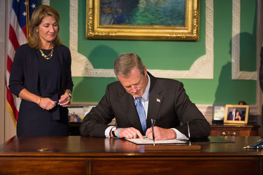 Gov. Charlie Baker signs the Fiscal Year 2016 budget on Friday at the State House, as Lt. Gov. Karyn Polito looks on. (Jesse Costa/WBUR)