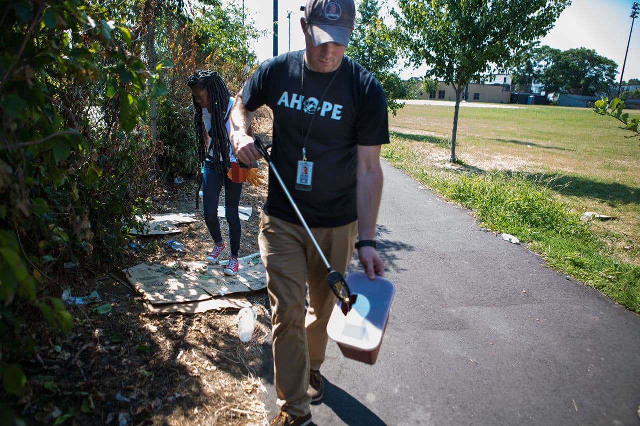 John Canty disposes of a syringe as Daphney Pacouloute continues her sweep of the bushes in Clifford Park. (Jesse Costa/WBUR)
