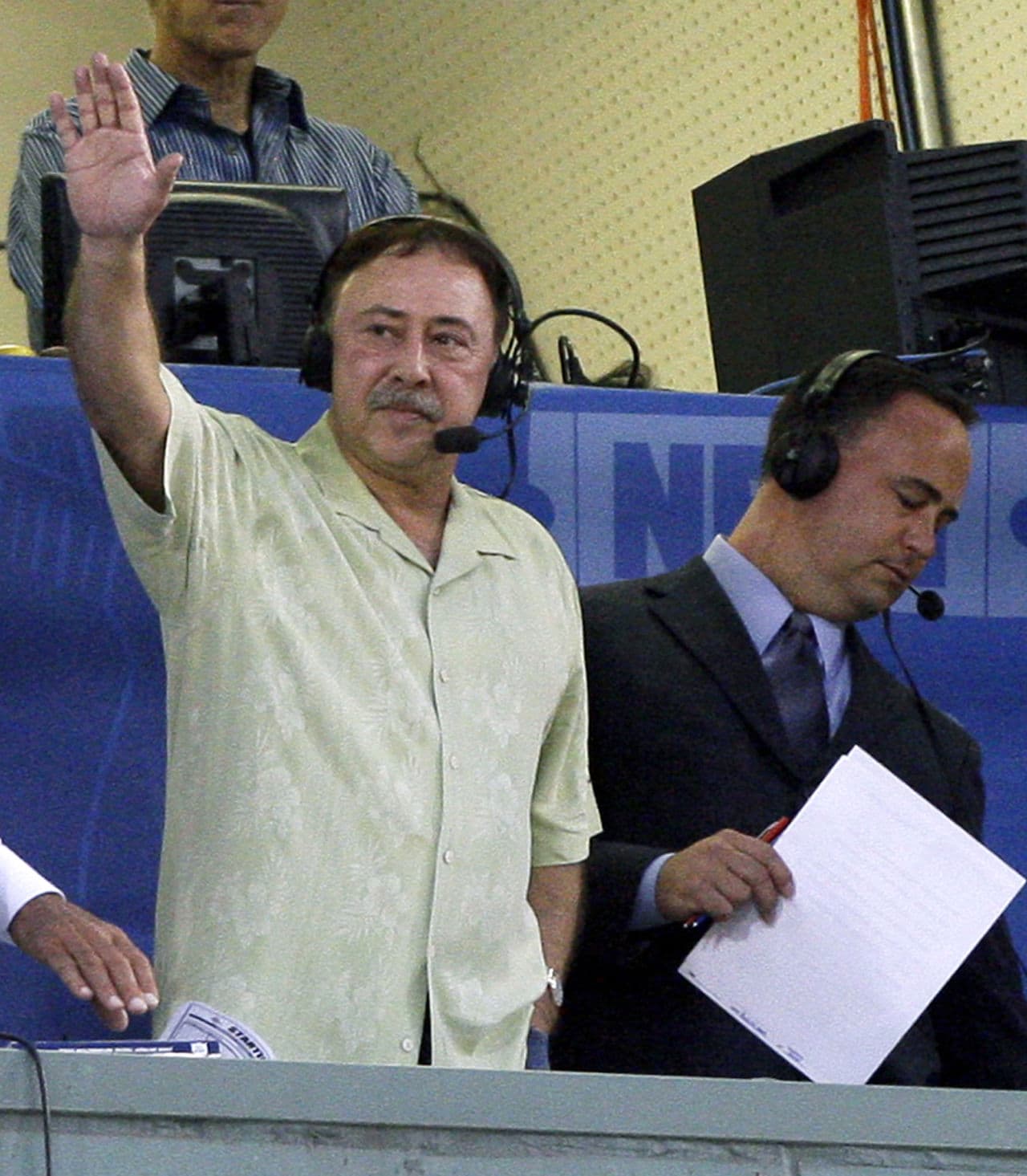 In this Aug. 12, 2009 file photo, Jerry Remy waves to the crowd from the television broadcast booth at Fenway Park. Don Orsillo is pictured to his right. (Elise Amendola/ AP)