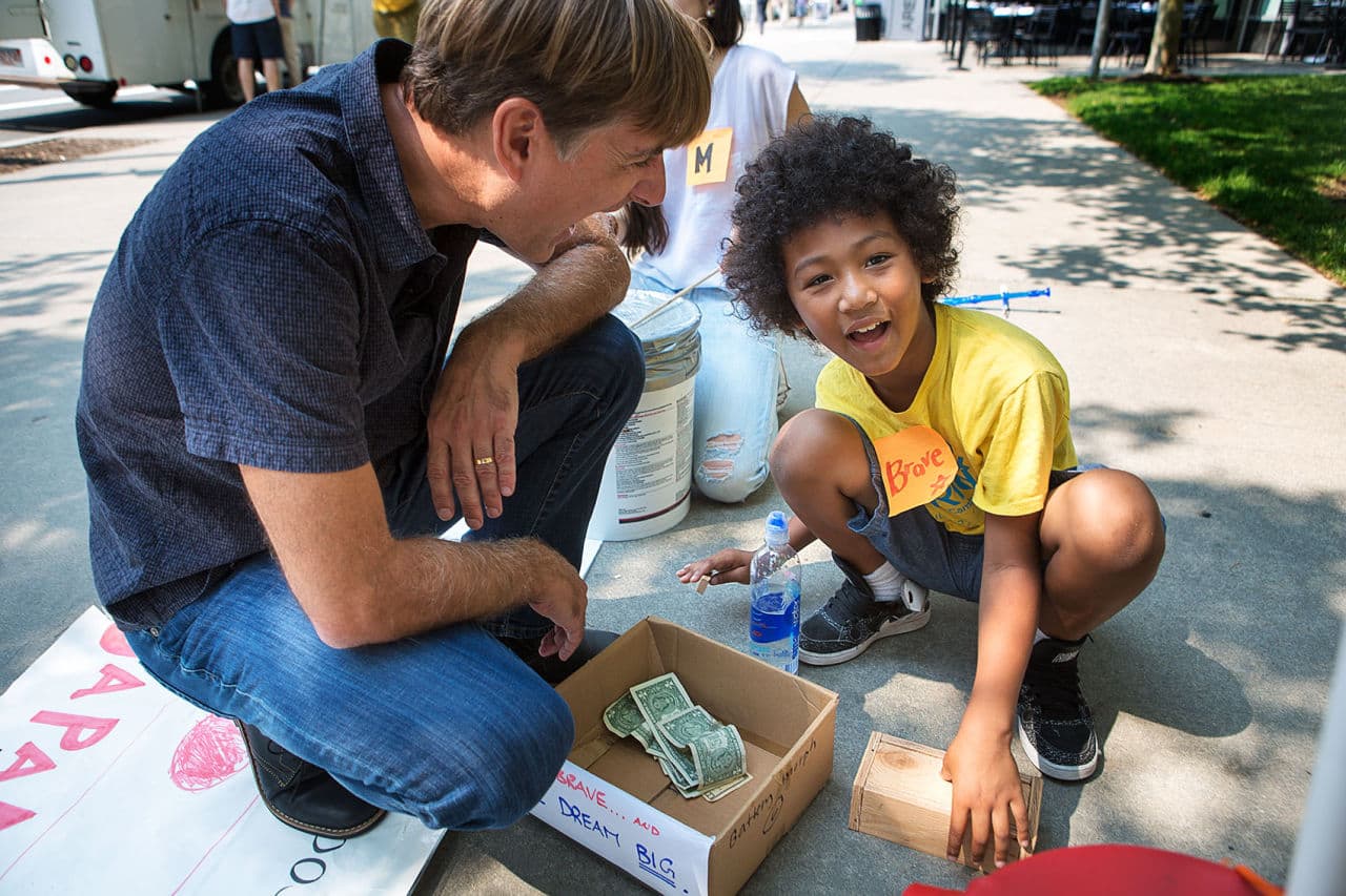 Matt Kressy, the head of MIT's IDM program, and Brave Sharab, 7, count how much money the group collected playing their homemade instruments in Cambridge's Technology Square. (Jesse Costa/WBUR)