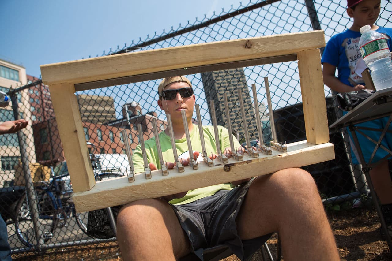 Ben Coble plays a chime instrument made of wood, metal tubing and wire on Carleton Street by the Kendall Square T station (Jesse Costa/WBUR)
