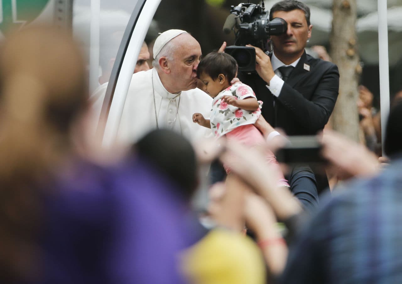 Pope Francis stops to kiss an unidentified child as he parades in the pope mobile on his way to celebrate Sunday Mass on the Benjamin Franklin Parkway in Philadelphia. (Pablo Martinez Monsivais/AP)