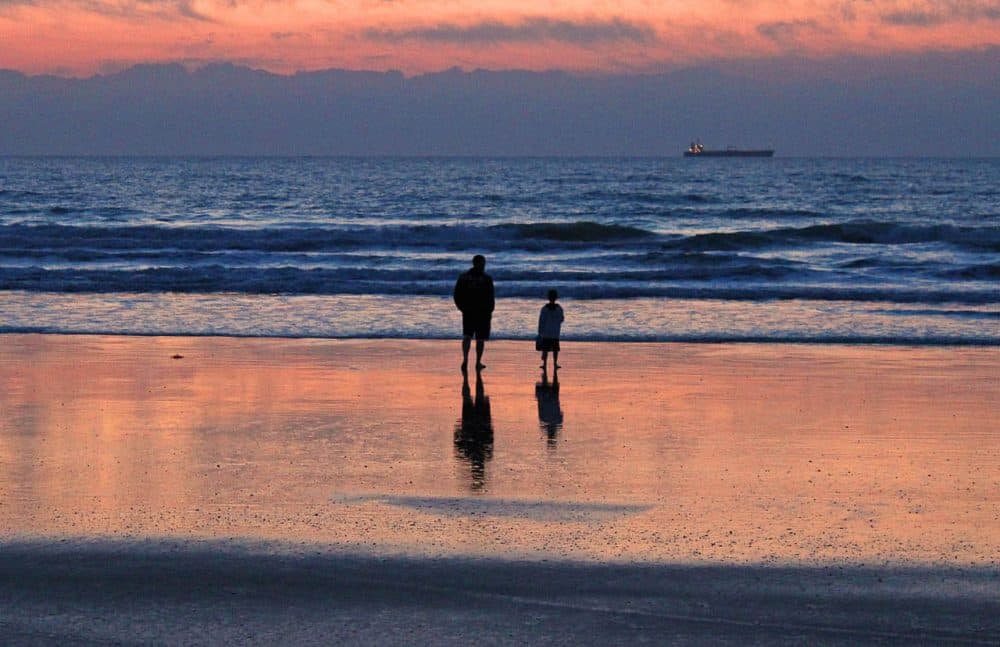 A father and son walk on the beach at sunset with a freighter in the distance. (bluecorvette/Flickr)