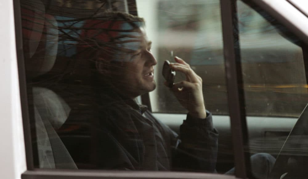 A driver talks on a cell phone while driving through the Financial District of Boston in 2011. The use of cellphones while driving has long been a source of contention in the state. Gov. Baker said he'd support a proposal to ban handheld use while driving. (Charles Krupa/AP)