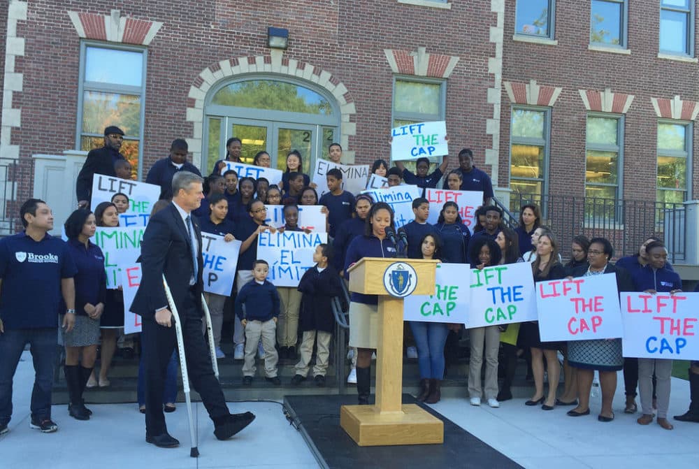 Gov. Charlie Baker, flanked by several schoolchildren holding signs, walks to announce proposed legislation on charter school caps. (Delores Handy/WBUR)