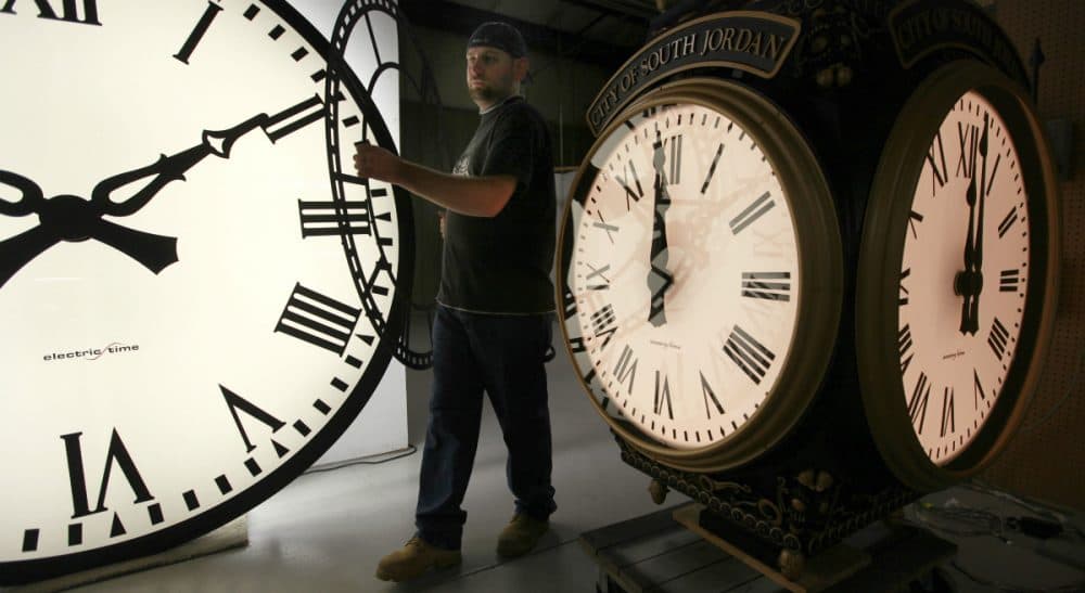 In this 2011 photo, Dan LaMoore of Electric Time Company moves a clock face at their plant in Medfield, Mass., between a large tower clock and a post clock. Daylight Savings Time ends at 2 a.m. on Sunday, Nov. 1, 2015, when clocks will be set back one hour. (Elise Amendola/AP)