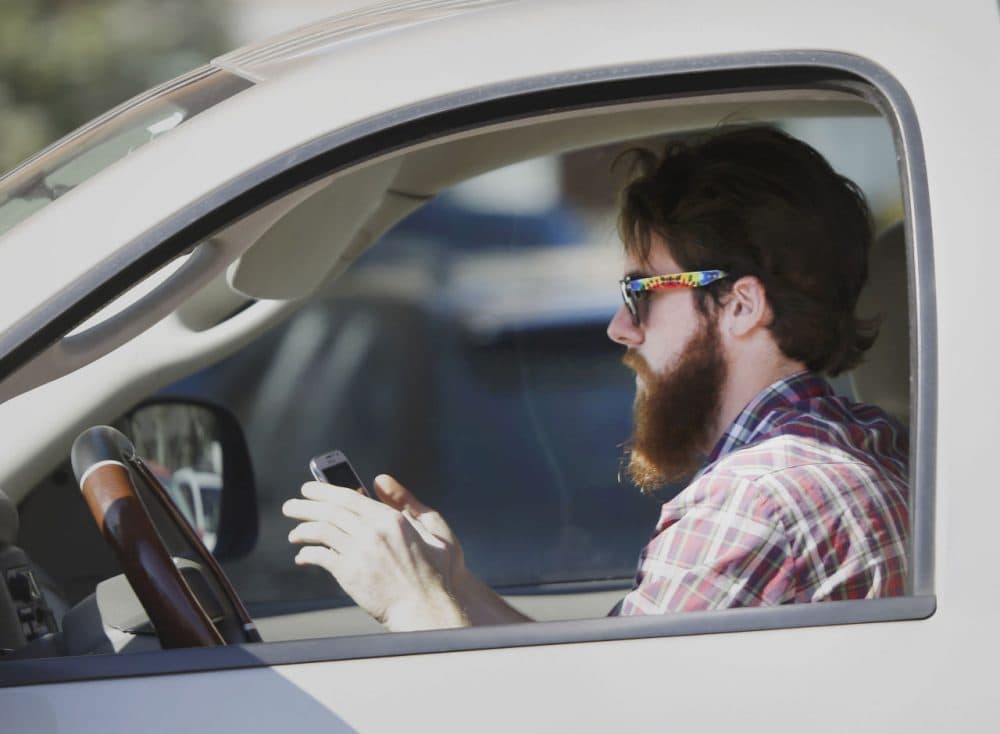 An man works his phone as he drives through traffic. (LM Otero/AP)