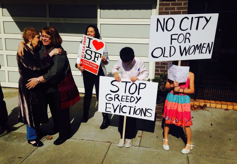 Outside Marilyn Fowler's apartment, neighbors hold signs protesting the cost of housing. (Peter O'Dowd)