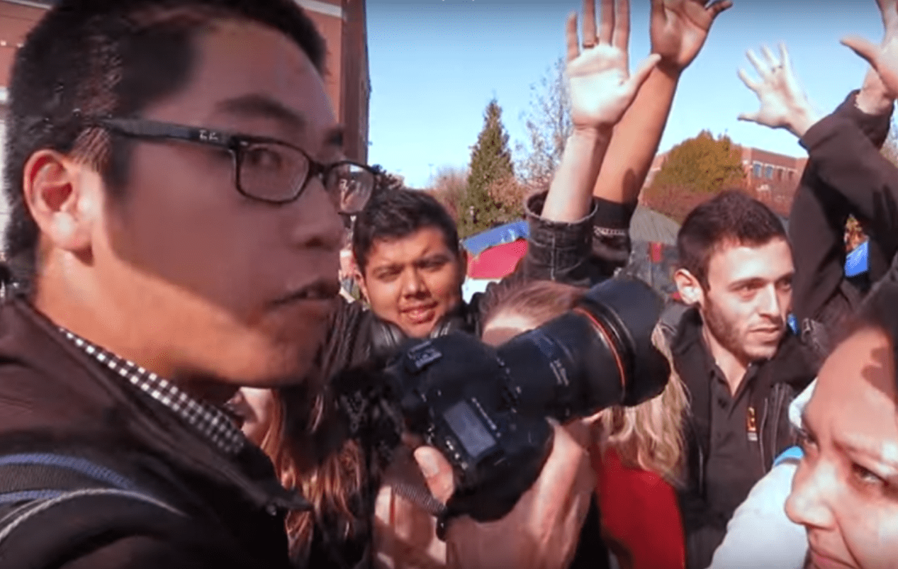 A screen grab from a video shot by student photographer Mark Schierbecker shows University of Missouri student photographer Tim Tai (left) and student protesters arguing over how close he is to them. (YouTube screen shot)