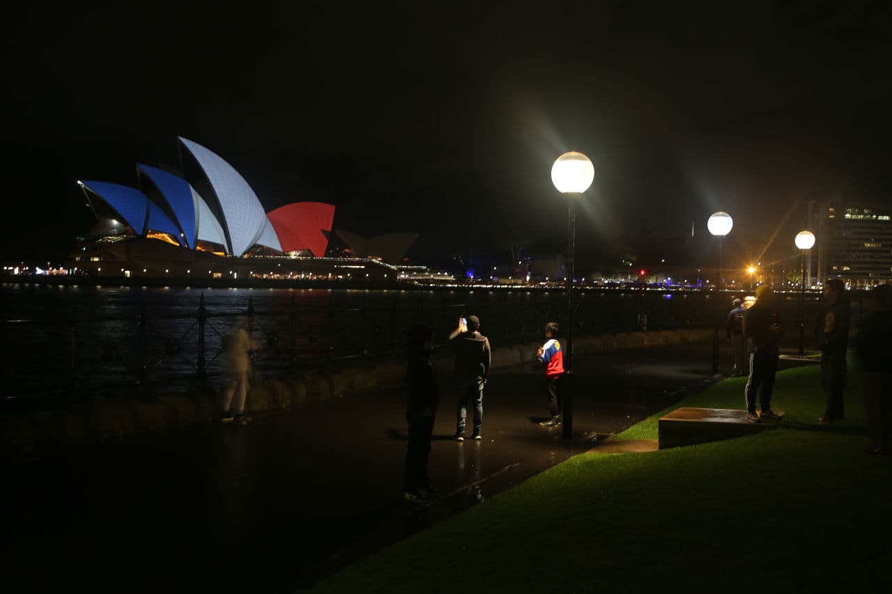 People stop to look at the sails of the Sydney Opera House that are lit in the colors of the French flag in Sydney. (Rick Rycroft/AP)