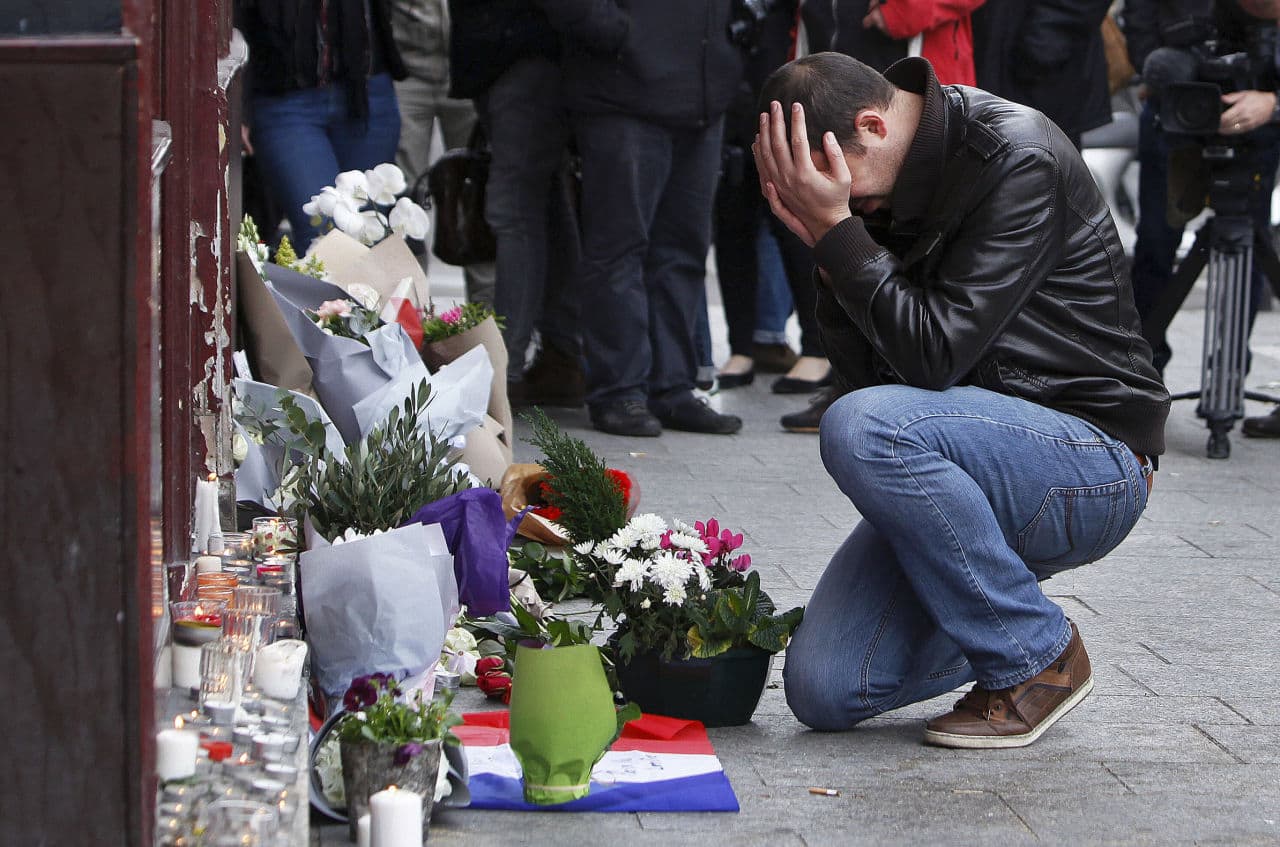 A man holds his head in his hands as he lays flowers in front of the Carillon cafe in Paris, the morning after coordinated attacks shook the city. (Thibault Camus/AP)