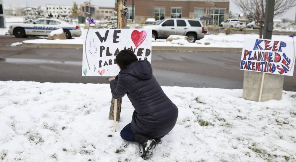 Bethany Winder, a nurse who lives in Colorado Springs, Colo., plants a sign in support of Planned Parenthood just south of its clinic as police investigators gather evidence near the scene of Friday's shooting at the clinic Sunday, Nov. 29, 2015, in northwest Colorado Springs. (David Zalubowski/ AP)