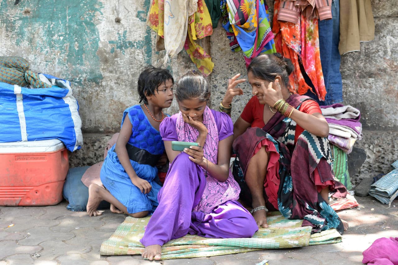 An Indian pavement dweller watches a movie on a mobile phone as others interact in Mumbai on June 3. (Indranil Mukherjee/AFP/Getty Images)