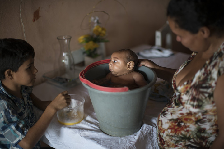 In this Dec. 23, 2015 photo, 10-year-old Elison, left, watches as his mother Solange Ferreira bathes Jose Wesley in a bucket at their house in Poco Fundo, Pernambuco state, Brazil. (AP Photo/Felipe Dana)