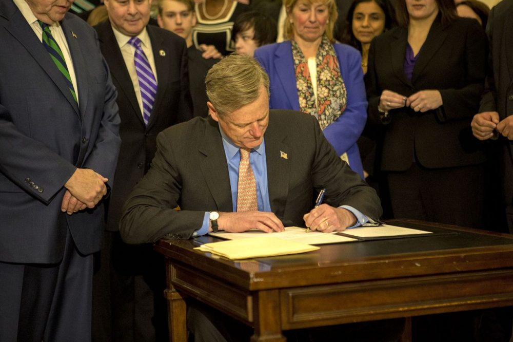 Surrounded by lawmakers and health and public safety officials, Gov. Charlie Baker signs the opioid bill into law on Monday at the State House. (Jesse Costa/WBUR)