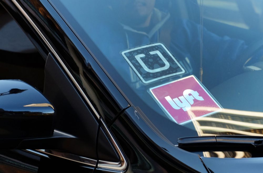 A driver displaying Lyft and Uber stickers on his front windshield drops off a passenger in downtown Los Angeles in January. (Richard Vogel/AP/File)