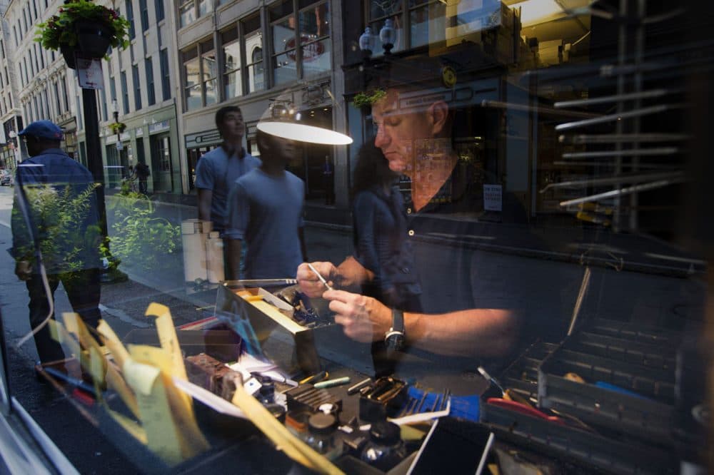 Bromfield Pen Shop's pen repair specialist Greg Byrne works in the on-street window as people pass by. (Jesse Costa/WBUR)