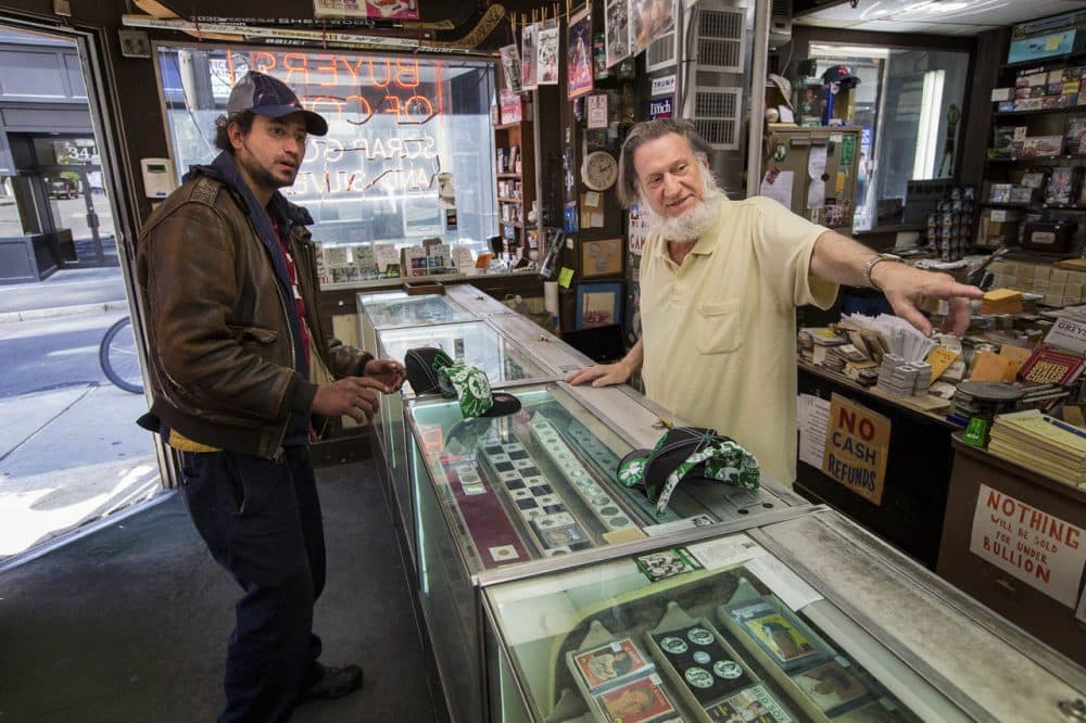 Bay State Coin Co. owner Andy Papertsian, right, makes a deal with William Gonzalez who is selling Boston Celtics hats. (Jesse Costa/WBUR)