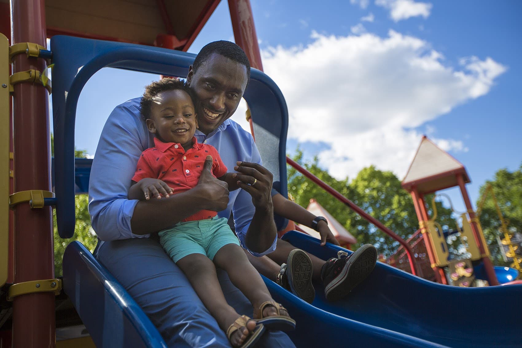 Charles Daniels, founder and CEO of the Boston-based nonprofit Fathers' Uplift, rides down a slide with his 1-year-old son Clayton in the Thetford Evans Playground in Dorchester. (Jesse Costa/WBUR)