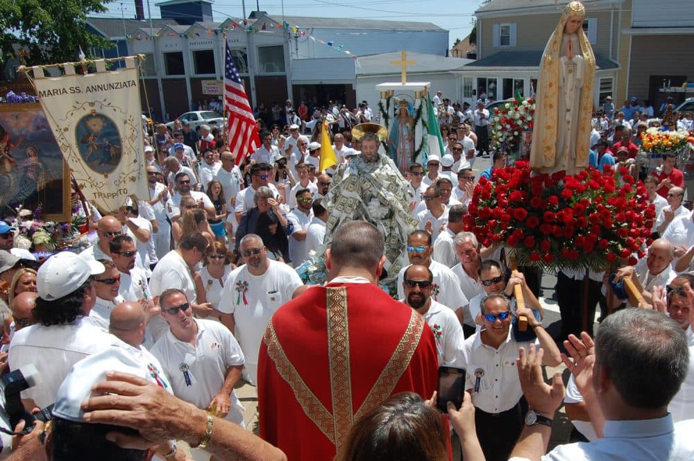 The statues and icons of saints are arrayed before Our Lady of Good Voyage Church as a priest leads the Sunday procession crowd in prayer, June 26, 2016. (Greg Cook)