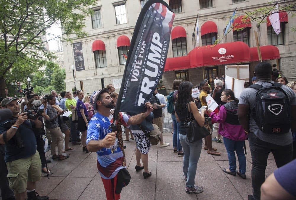 A Trump supporter walks through the protesters carrying a &quot;Vote for Trump&quot; banner. (Joe Difazio for WBUR)