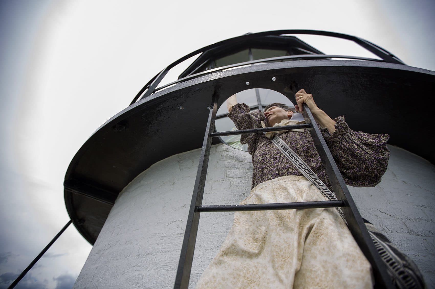 Sally Snowman climbs a ladder to the top of Boston Light. (Jesse Costa/WBUR)
