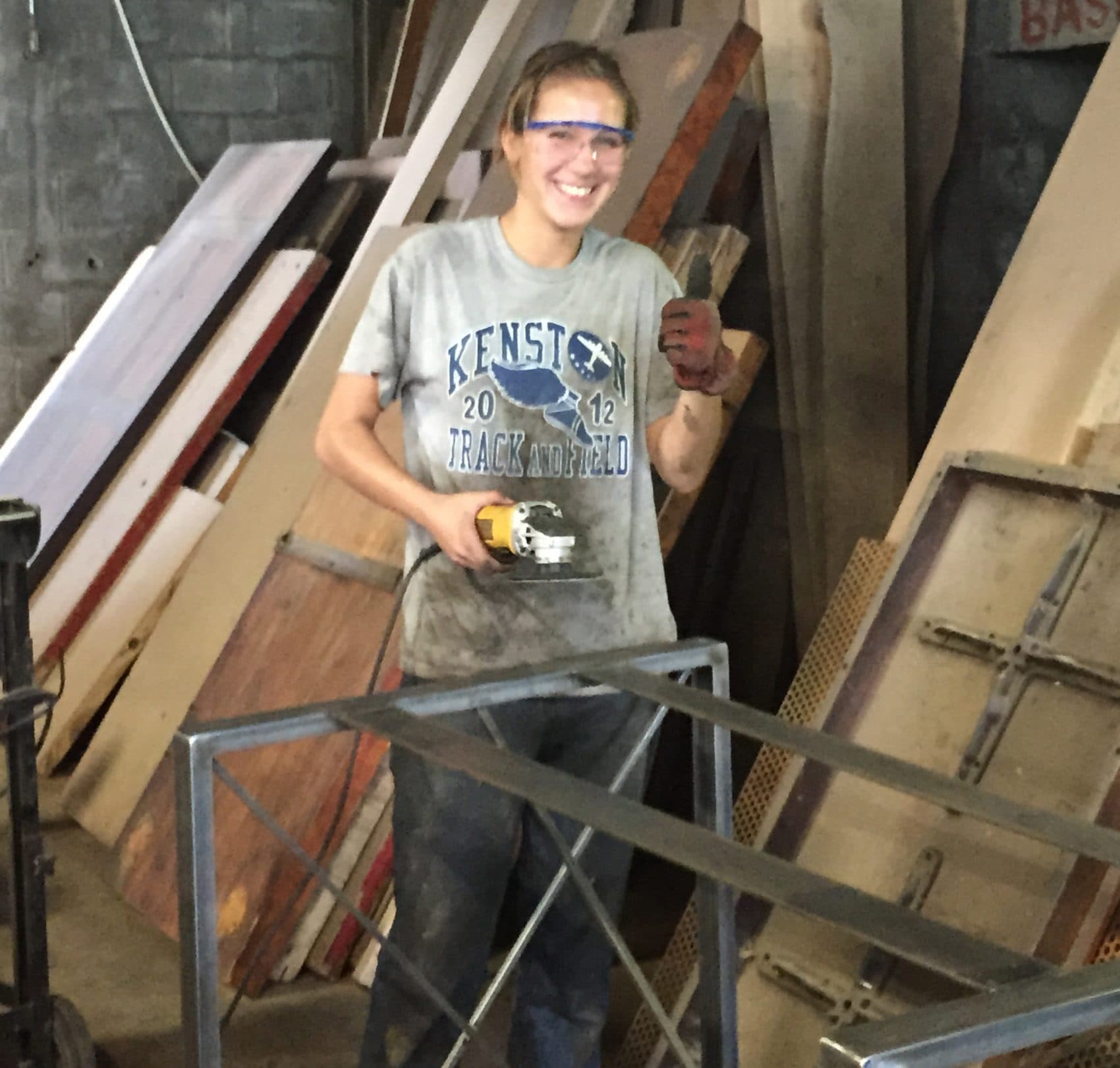 A Cleveland Arts worker smiles while working with a sander tool in the workshop. (Robin Young/Here &amp; Now)