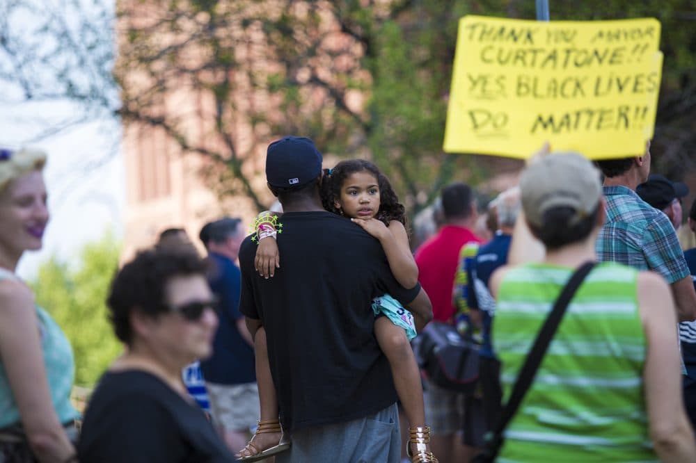 Lianne Curtis holds a yellow sign that thanks Mayor Curtatone for allowing the Black Lives Matter sign to stay above City Hall. Mike F. holds his 7-year-old daughter Audrey nearby. (Jesse Costa/WBUR)