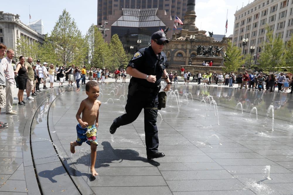 An Indiana state police officer runs through a fountain with a child in Cleveland's Public Square on Thursday. (Alex Brandon/AP)