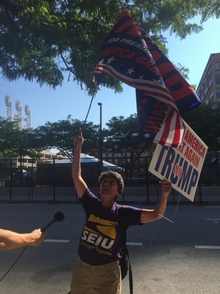 Moriem Noujaim, a Donald Trump supporter from California, holds a sign and a flag outside the Quicken Loans Arena during the Republican National Convention. (Robin Young/Here &amp; Now)
