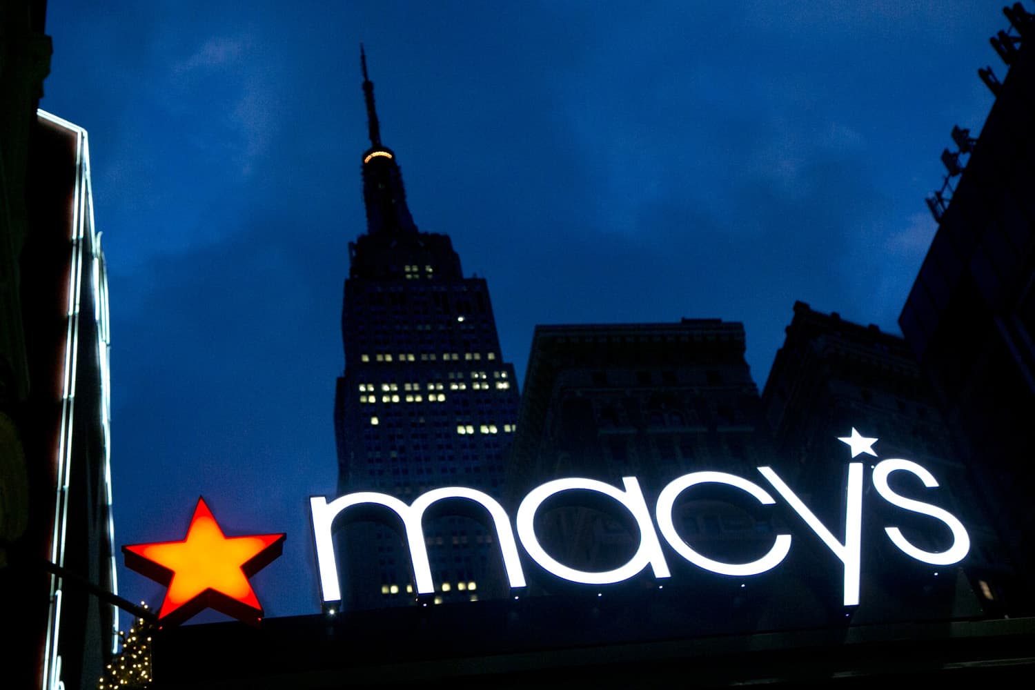 In this Nov. 21, 2013, file photo, with the Empire State building in the background, the Macy's logo is illuminated on the front of the department store in New York. (Mark Lennihan, File/AP)