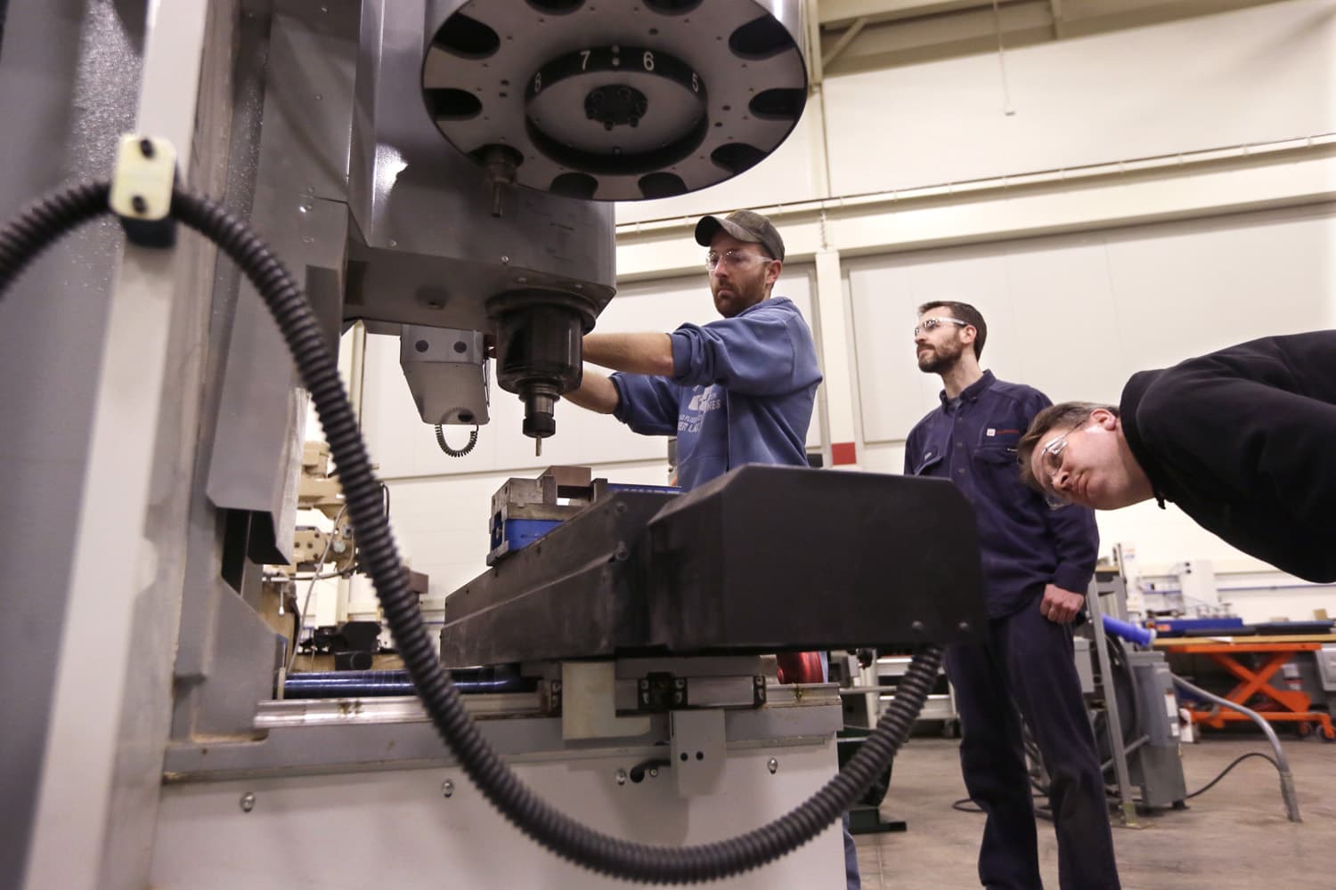 In a photo from Wednesday, Feb. 11, 2015 in Lansing, Mich., Lansing Community College, Brad Bancroft, left, operates a mill as Nate Joseph, center, and Adam Woodhams, right, look on in the advanced precision machining class. (Carlos Osorio/AP)