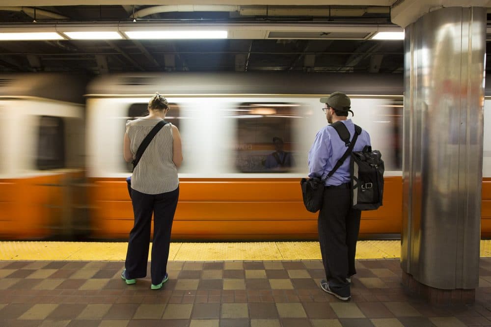 Commuters wait on the platform as an Orange Line train enters Downtown Crossing station. (Jesse Costa/WBUR)