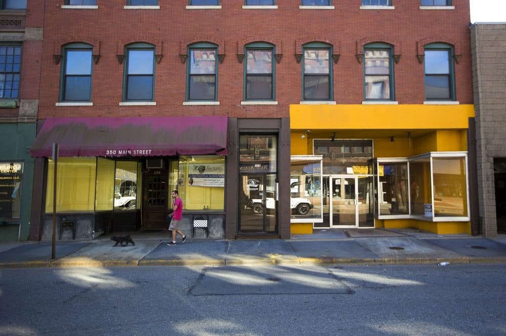 A man walks his dog in front of vacant commercial spaces along Main Street in Fitchburg. (Jesse Costa/WBUR)