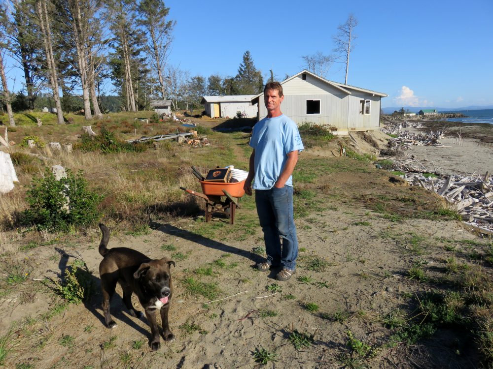 Homeowner Tom Burchard -- with his dog Bo -- has an air of resignation about soon losing the waterfront property that he said he picked up cheap. (Tom Banse/Northwest News Network)