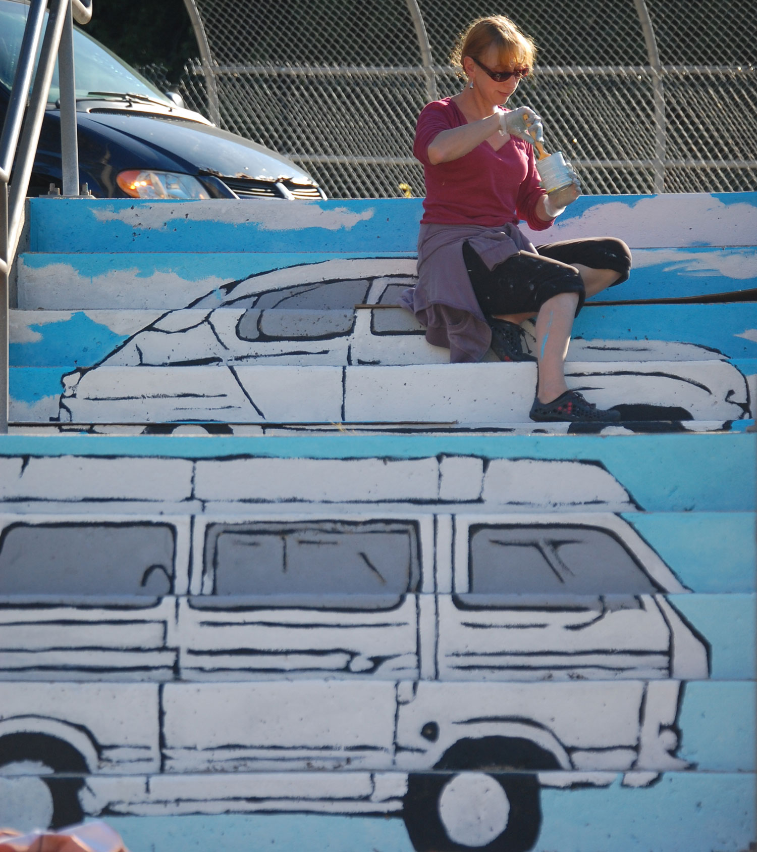 Liz LaManche paints “The Soul’s Journey as a Series of Weird Old Automobiles" in the park at the intersection of Pearl and Medford streets in Somerville. (Greg Cook)