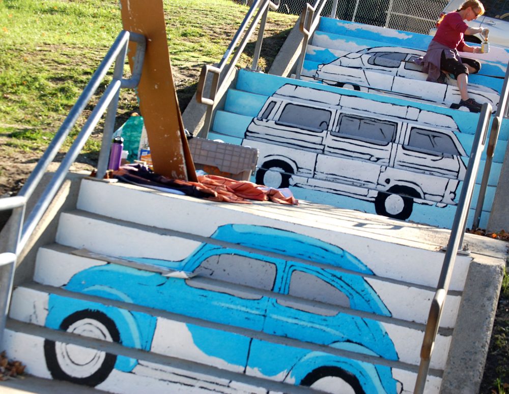 Liz LaManche paints “The Soul’s Journey as a Series of Weird Old Automobiles&quot; in the park at the intersection of Pearl and Medford streets in Somerville. (Greg Cook)