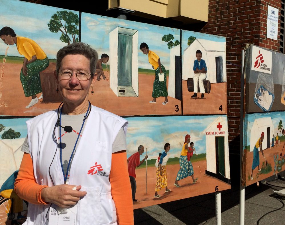 Dr. Chloe Wurr stands in front of the display in Boston that shows a tool doctors use to explain symptoms of diseases like cholera and malaria to people who cannot read. (Qainat Khan for WBUR)