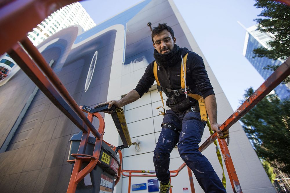 Mehdi Ghadyanloo climbs into a cherry picker to begin painting a mural on the wall in Dewey Square on Friday, Oct. 14. (Jesse Costa/WBUR)
