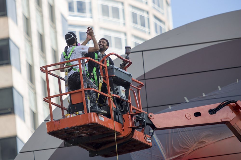 Mehdi Ghadyanloo and his assistant Henry Kunkel high five after the completion of the bolloon at the top of the mural. (Jesse Costa/WBUR)