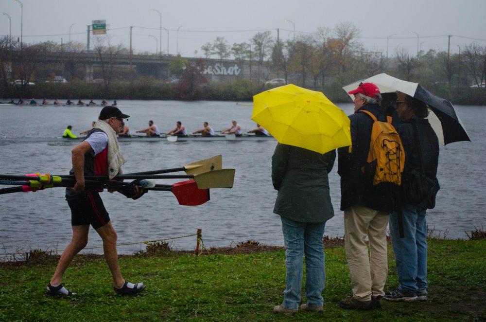 Spectators stand under their umbrellas by the Riverside Boat Club in Cambridge on the first day of the Head of the Charles. (Elizabeth Gillis/WBUR)