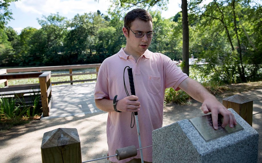 Perkins student Tom Pelletier reads from an information marker about fish in the Charles River on the Watertown braille trail. (Robin Lubbock/WBUR)